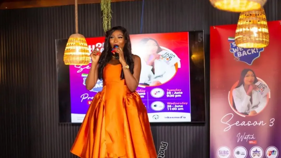 Stella Bangura holding a microphone in an orange dress